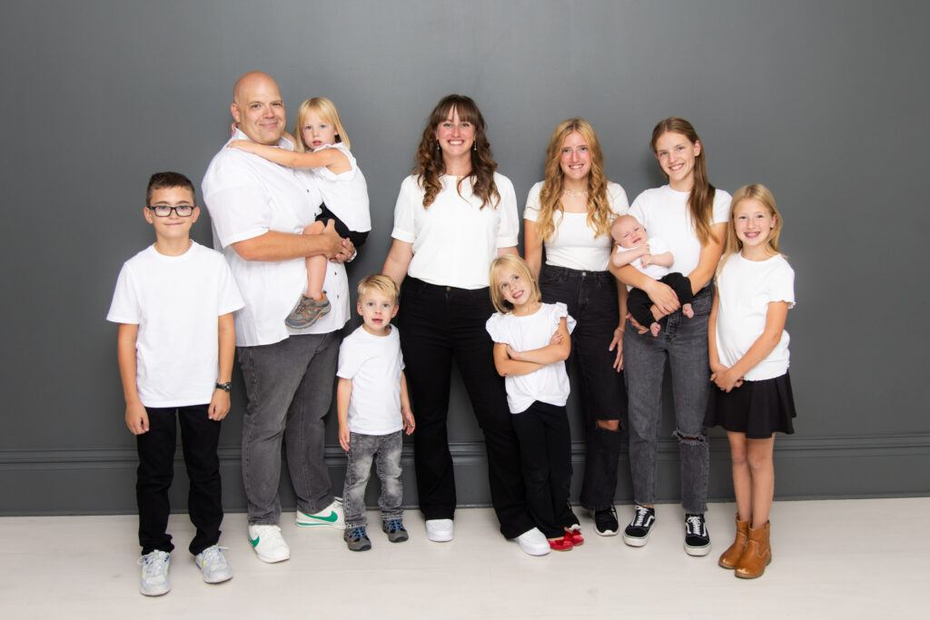 Family picture of 10 people - mom, dad, and 8 children, ages 14 to newborn, all wearing white tops and black pants.